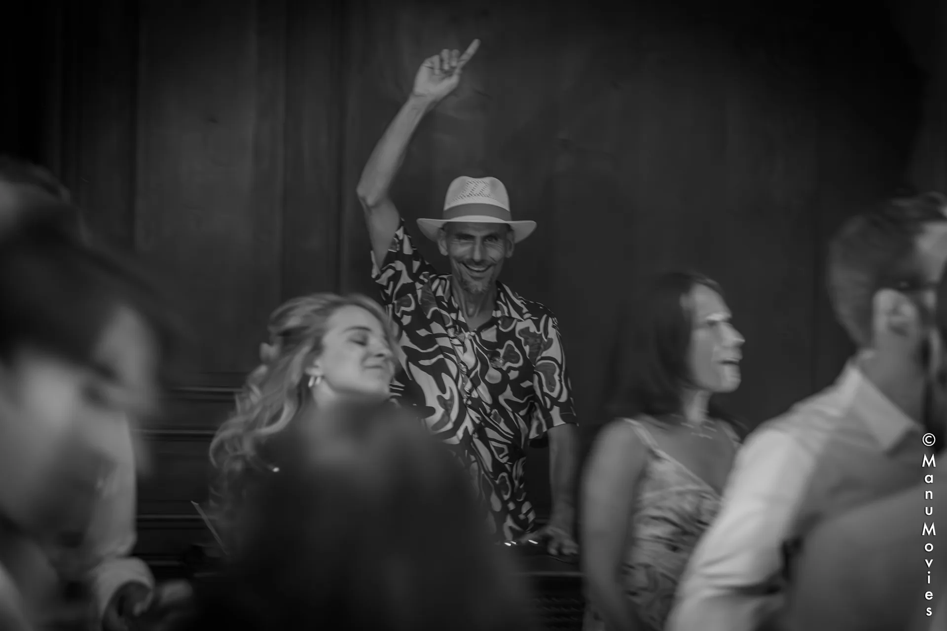 mikOsax, bras levé au milieu des danseurs pendant un mariage à Paris (photo noir et blanc)