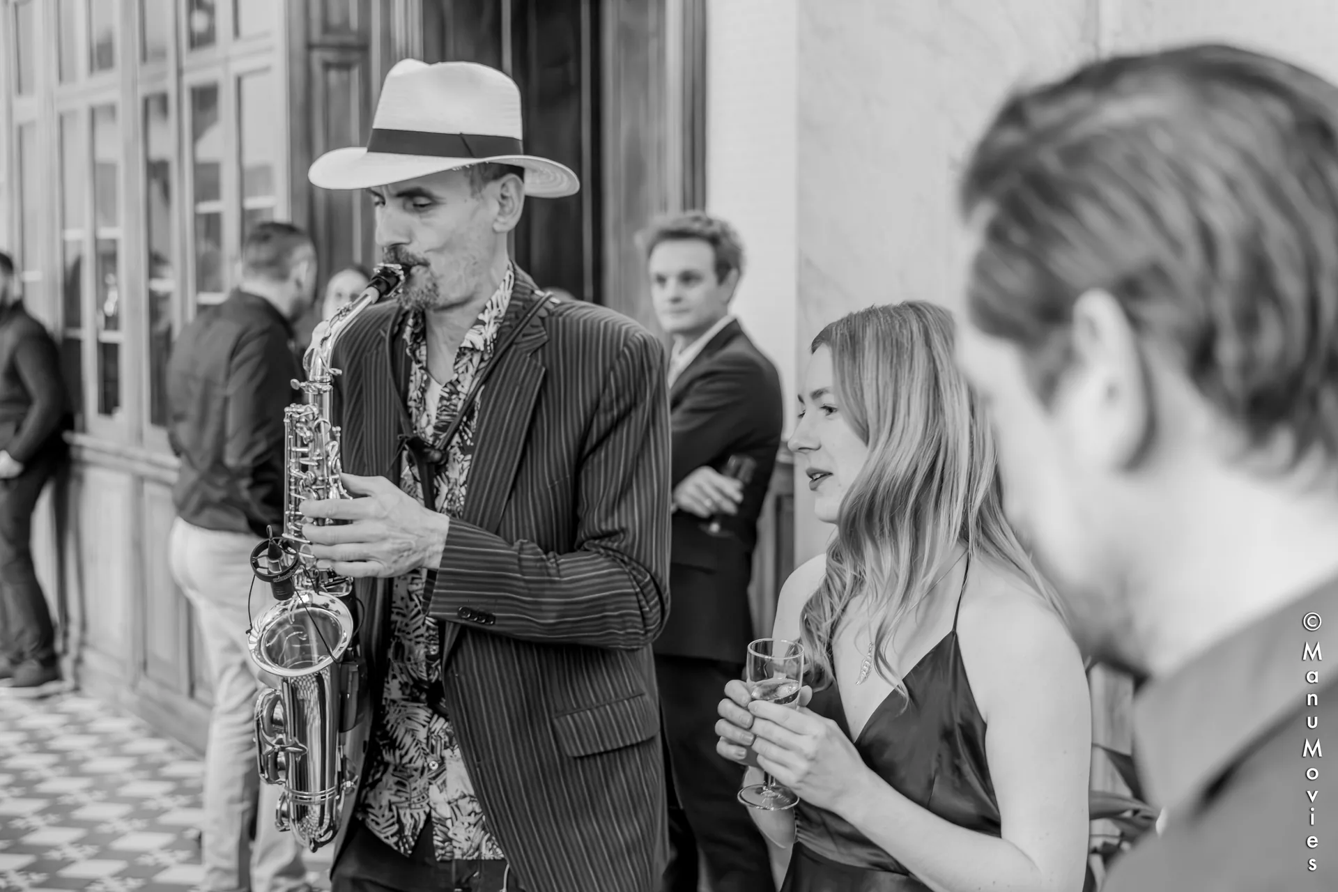 mikOsax, saxophoniste à Paris, joue en costume rayé et panama lors d'un cocktail chic (photo noir et blanc)