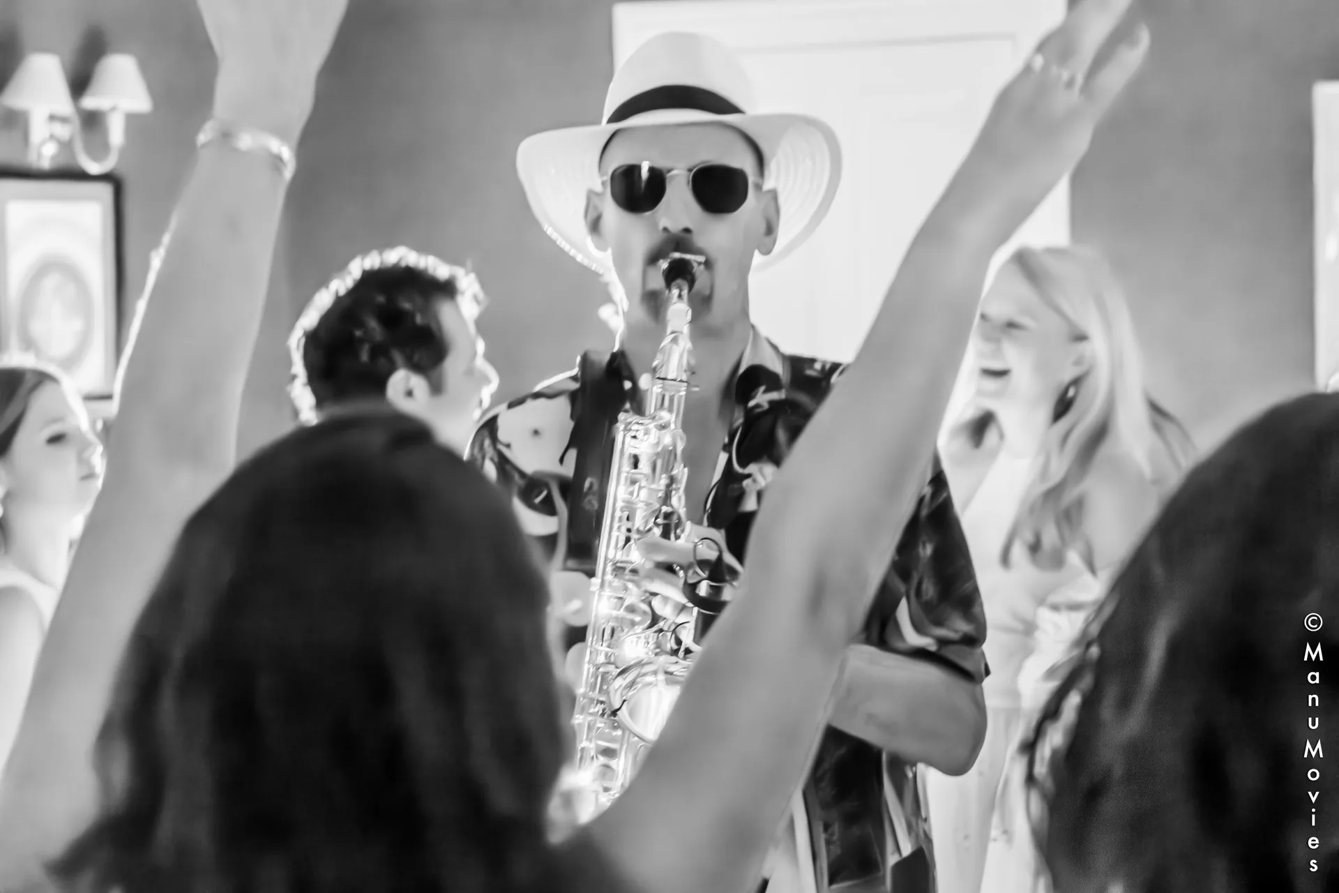 Les invités lèvent les bras autour du saxophoniste mikOsax pendant une soirée en Île-de-France (photo noir et blanc)